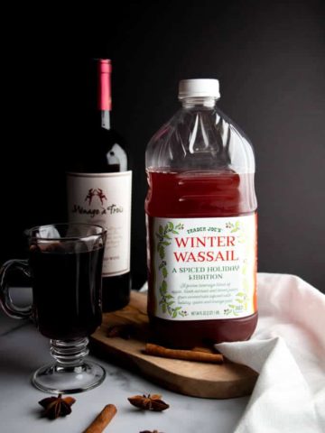 A bottle of Trader Joe's Winter Wassail next to wine, spices and a finished mulled win
