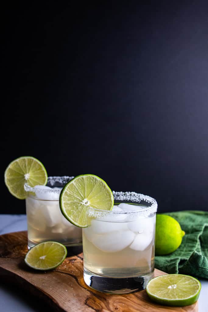 Two finished Spicy Jalapeno Limeade Margarita garnished with limes