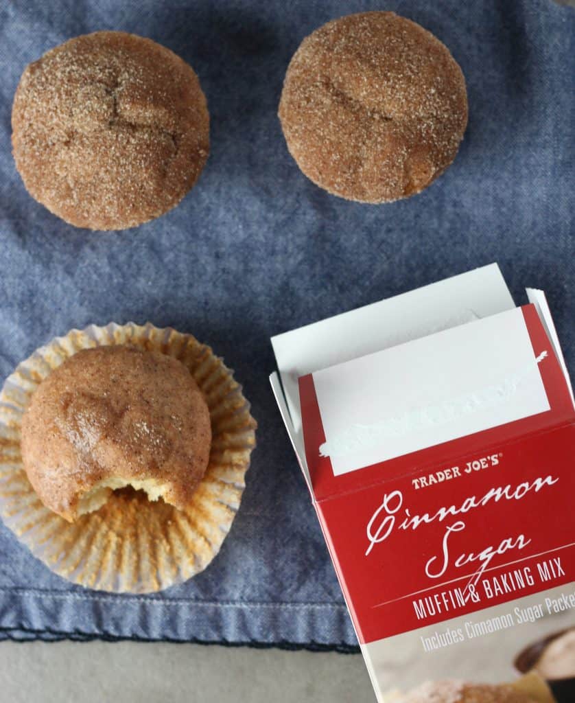 Trader Joe's Cinnamon Sugar Muffin and Baking Mix after being baked in which three muffins are pictured. One with a bite out of it on a blue napkin.