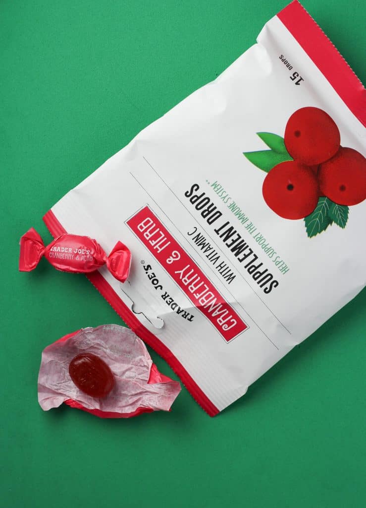 Trader Joe's Cranberry and Herb Supplement Drops showing one wrapped and one unwrapped drop next to the bag on a green background.