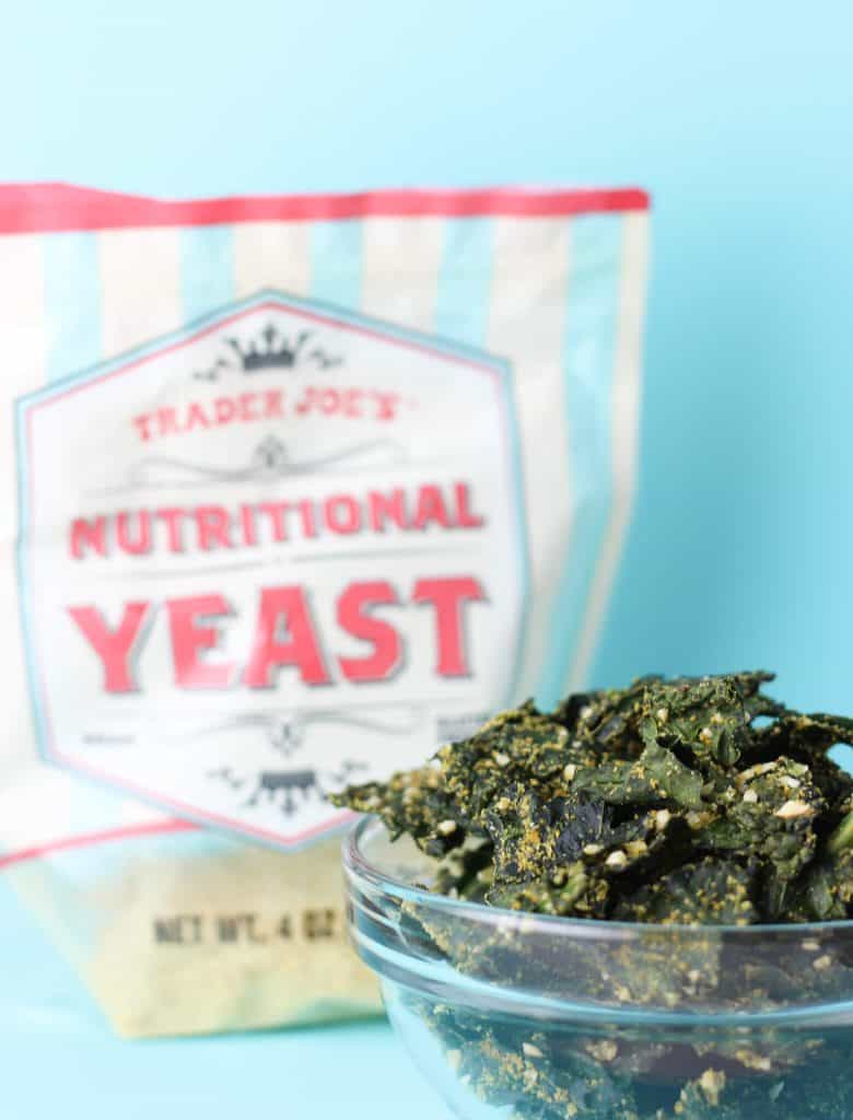 Trader Joe's Nutritional Yeast with kale chips in the front on a blue background