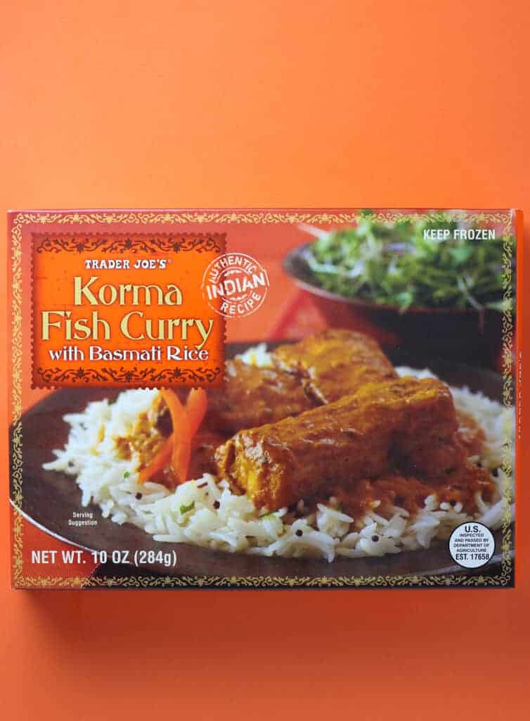 An unopened box of Trader Joe's Korma Fish Curry box as sold in stores on an orange background