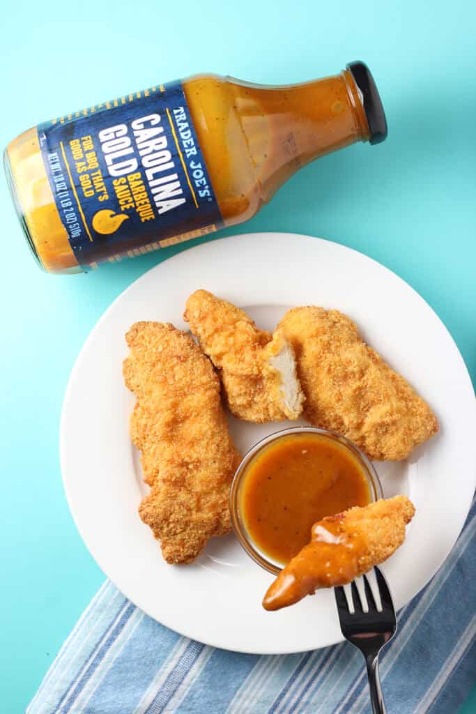 Trader Joe's Carolina Gold Barbeque Sauce next to chicken on a white plate and blue background.