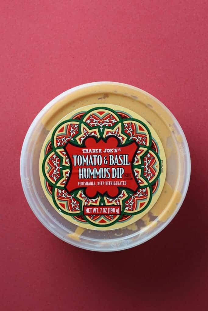 Trader Joe's Tomato and Basil Hummus Dip on a red background.