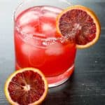 A blood orange margarita with garnish on a dark wooden surface
