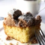 A slice of crumb cake with powdered sugar and a coffee cup in the background