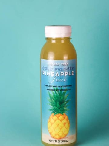 An unopened bottle of Trader Joe's Cold Pressed Pineapple Juice with a blue background.
