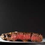 A medium rare rib eye steak cut to show off the pink center. This is on a cutting board on a marble surface with a black background