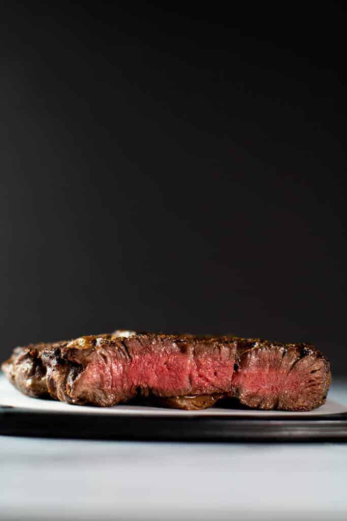 A medium rare rib eye steak cut to show off the pink center. This is on a cutting board on a marble surface with a black background