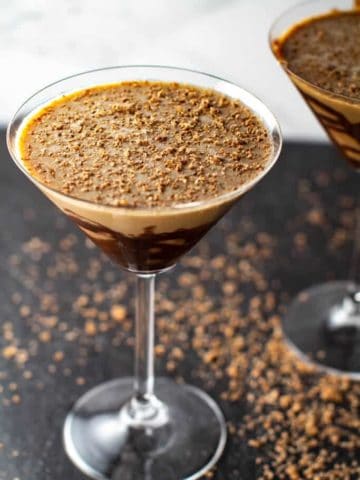 A close up of two chocolate martinis with chocolate shavings on the black surface