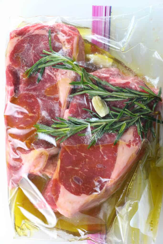 Two Ribeye Steaks marinating in a bag with olive oil, rosemary, and garlic
