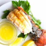 A fully cooked lobster tail with lemon, parsley, and melted butter on a white plate