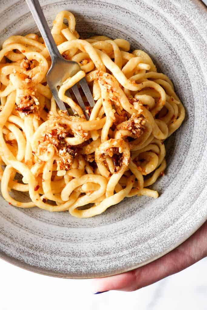 The author holding a bowl of linguine covered in chili onion crunch