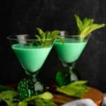 Two finished Grasshopper cocktails on a dark surface garnished with mint leaves.