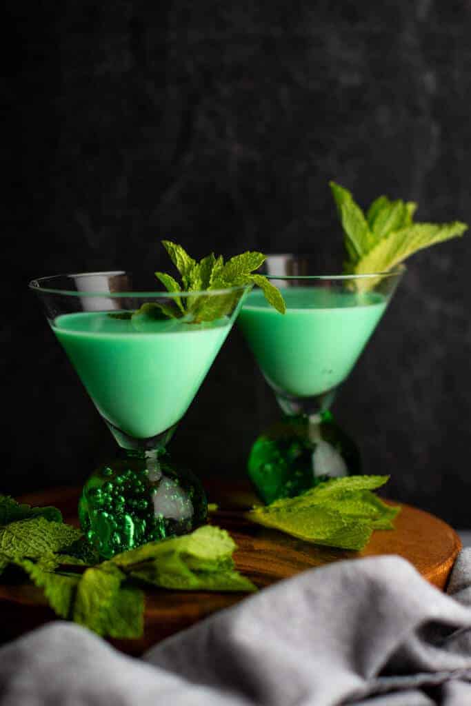 Two finished Grasshopper cocktails on a dark surface garnished with mint leaves.
