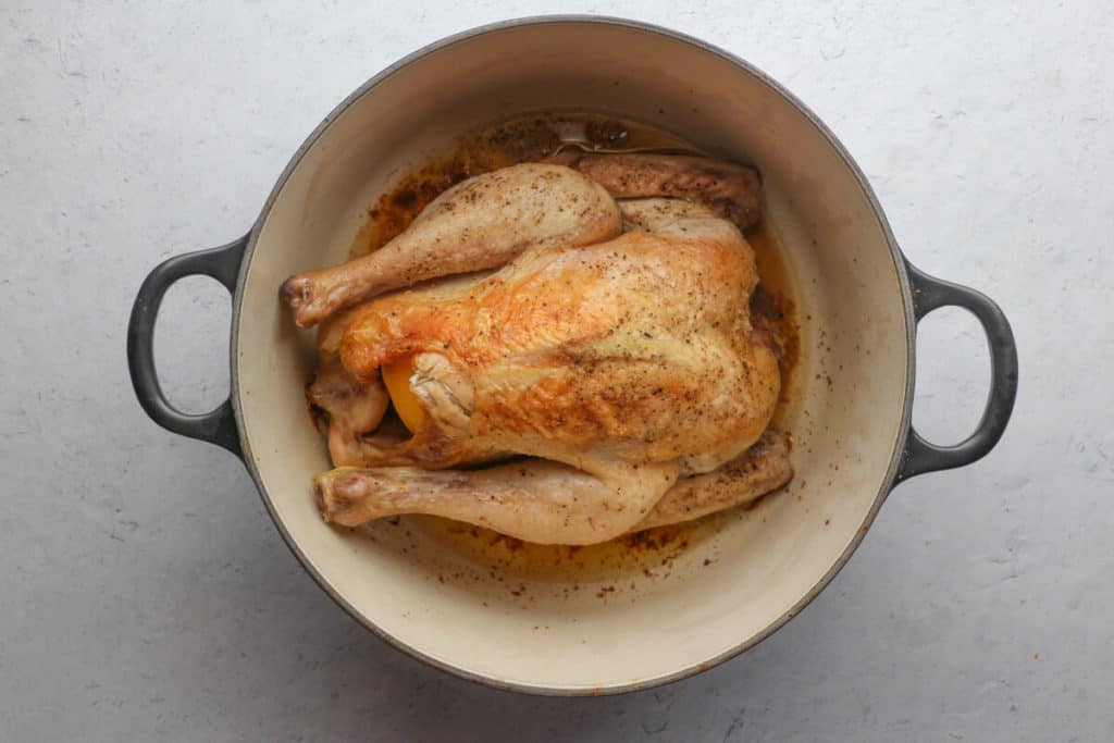 A fully cooked Trader Joe's All Natural Heirloom Whole Chicken in a black dutch oven