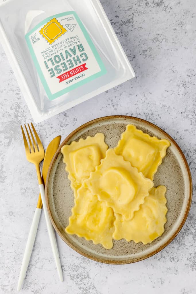 Five fully cooked Trader Joe's Gluten Free Cheese Ravioli on a plate with the box off to the side.