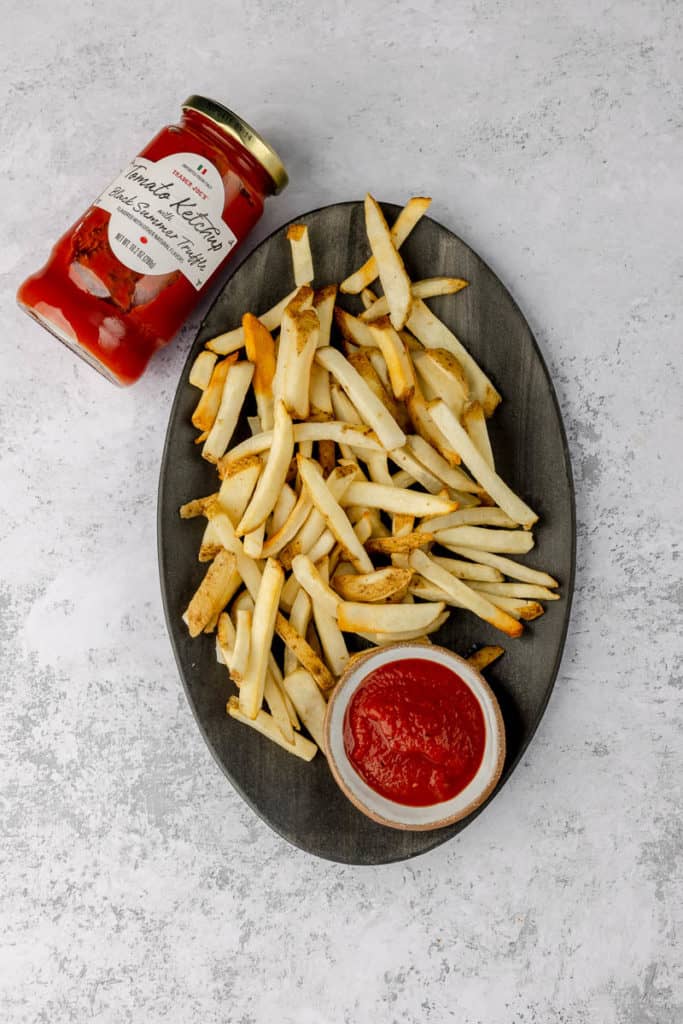 Trader Joe's Tomato Ketchup with Black Summer Truffle with a plate of fries on a grey surface.