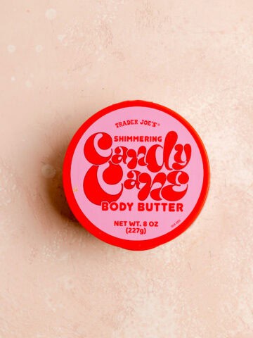 Trader Joe's Candy Cane Shimmering Body Butter unopened on a pink surface.