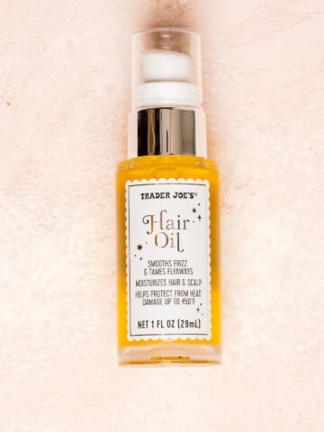 An unopened bottle of Trader Joe's Hair Oil on a pink surface.