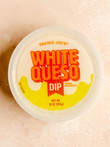 A new package of Trader Joe's White Queso Dip on a pink surface.