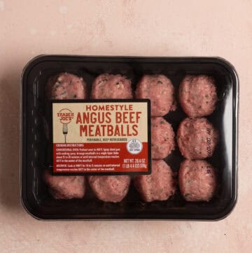 An unopened package of Trader Joe's Homestyle Angus Beef Meatballs on a pink surface.