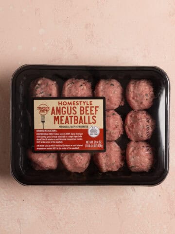 An unopened package of Trader Joe's Homestyle Angus Beef Meatballs on a pink surface.