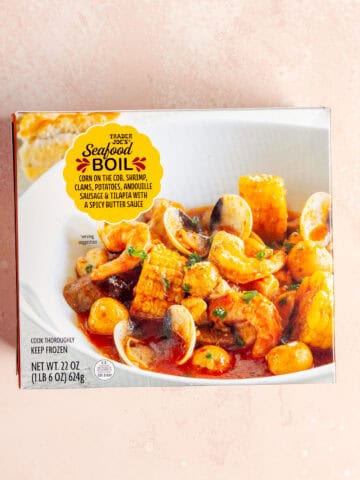 An unopened box of Trader Joe's Seafood Boil on a pink surface.