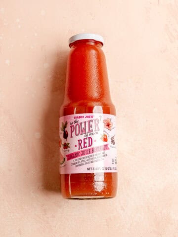 An unopened bottle of Trader Joe's To The Power of Seven Red Organic Juice Beverage on a pink surface.