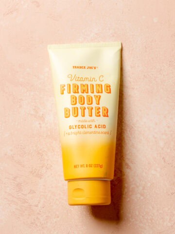 An unopened tube of Trader Joe's Vitamin C Firming Body Butter on a pink surface.