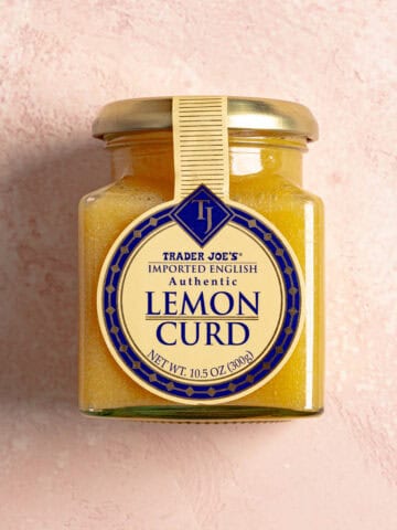 An unopened jar of Trader Joe's Lemon Curd on a pink surface.