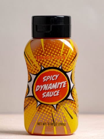 Trader Joe's Spicy Dynamite Sauce upright on a pink surface and grey background.