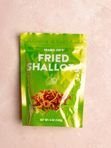 An unopened bag of Trader Joe's Fried Shallots on a pink surface.