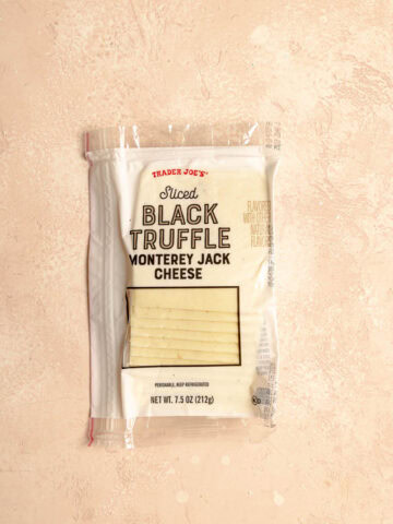 An unopened package of Trader Joe's Sliced Black Truffle Monterey Jack Cheese on a pink surface.