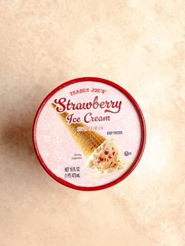 An unopened container of Trader Joe's Strawberry Ice Cream on a pink surface.