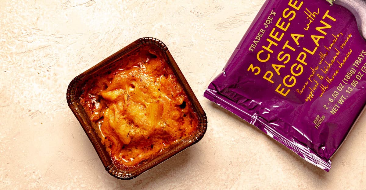 A fully heated portion of Trader Joe's 3 Cheese Pasta with Eggplant on a pink surface with the original wrapper.