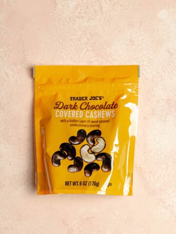 An unopened bag of Trader Joe's Dark Chocolate Covered Cashews on a pink surface.