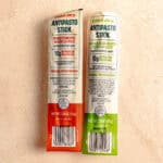 Two unopened Trader Joe's Antipasto Sticks on a pink surface.