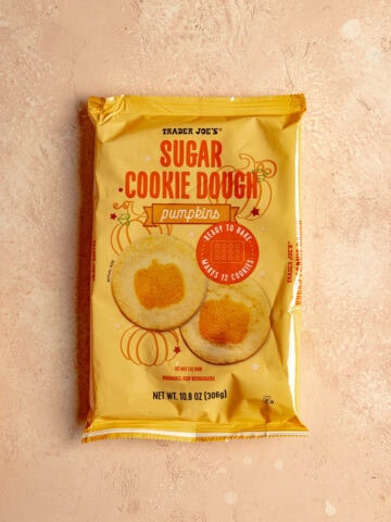 An unopened package of Trader Joe's Sugar Cookie Dough Pumpkins on a pink surface.