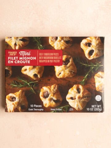 An unopened box of Trader Joe's Mini Filet Mignon en Croute on a pink surface.