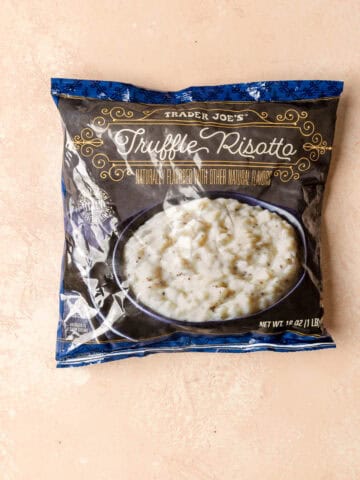 An unopened bag of Trader Joe's Truffle Risotto on a pink surface.