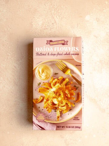 An unopened box of Trader Joe's Onion Flowers on a pink surface.