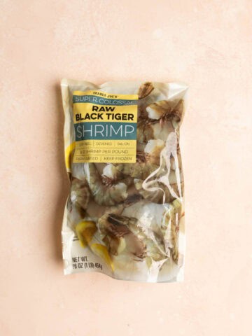 Trader Joe's Super Colossal Raw Black Tiger Shrimp in an unopened bag on a pink surface.