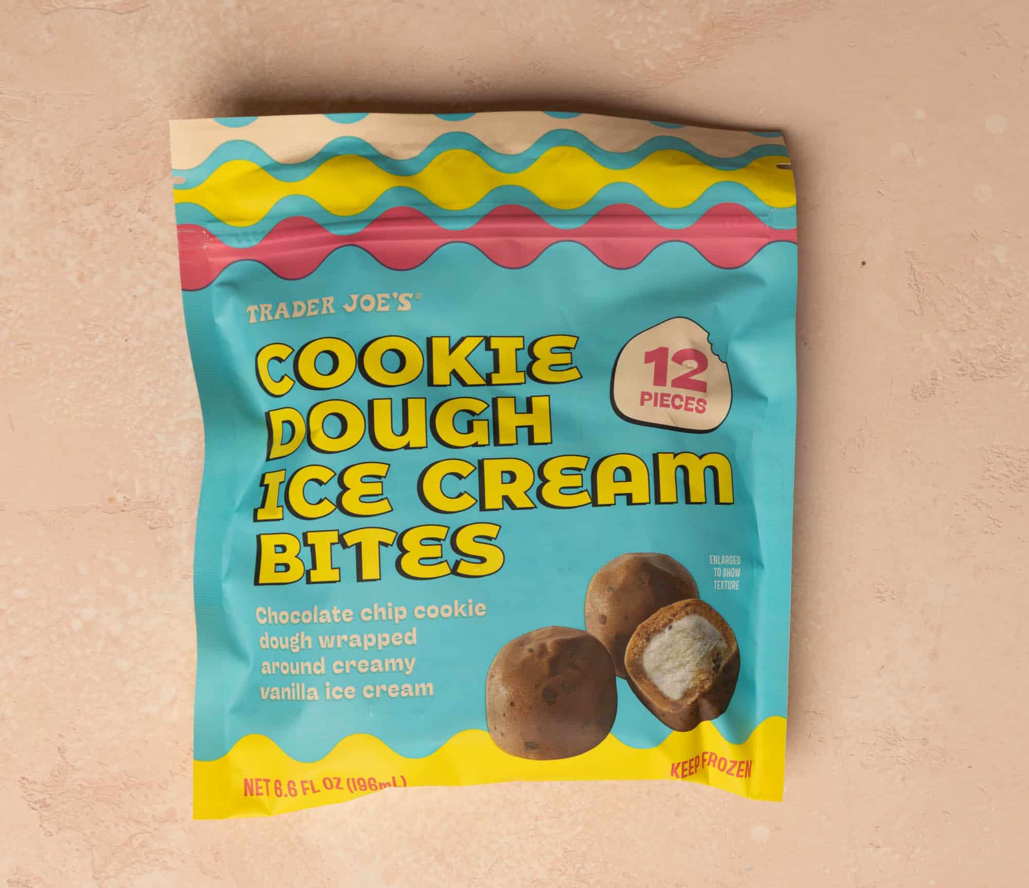 An unopened bag of Trader Joe's Cookie Dough Ice Cream Bites on a pink surface.
