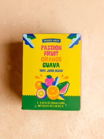An unopened box of Trader Joe's Passion Fruit Orange Guava Juice on a pink surface.