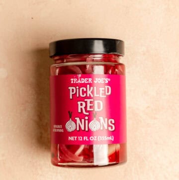 An unopened jar of Trader Joe's Pickled Red Onions on a pink surface.