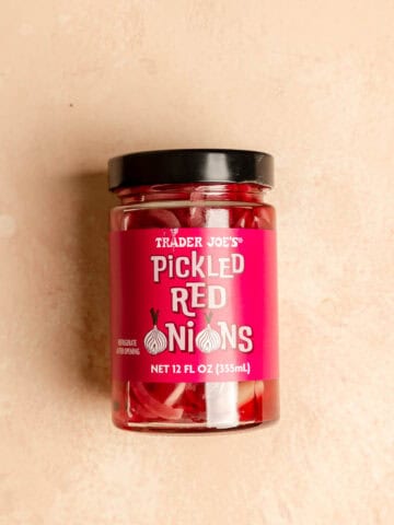 An unopened jar of Trader Joe's Pickled Red Onions on a pink surface.