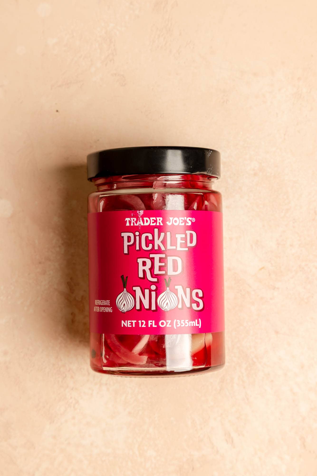 An unopened jar of Trader Joe's Pickled Red Onions on a pink surface.