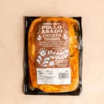 An unopened package of Trader Joe's Pollo Asado Chicken Thighs on a pink surface.