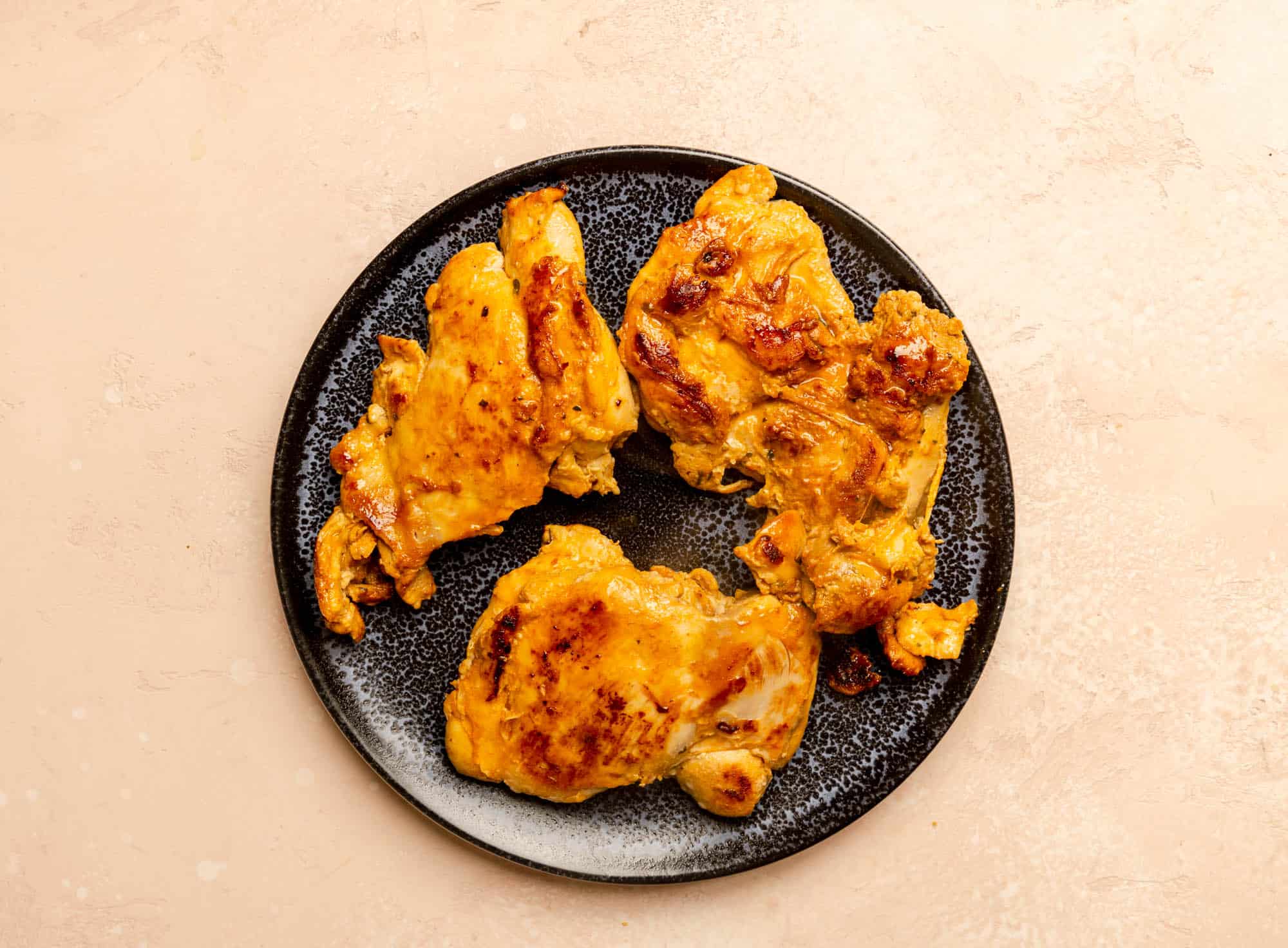 A plate of fully cooked Trader Joe's Pollo Asado Chicken Thighs on a pink surface.